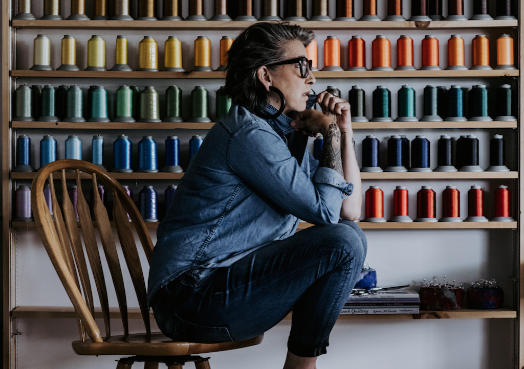 Karen McTavish sitting on a chair in front of colored spools of thread